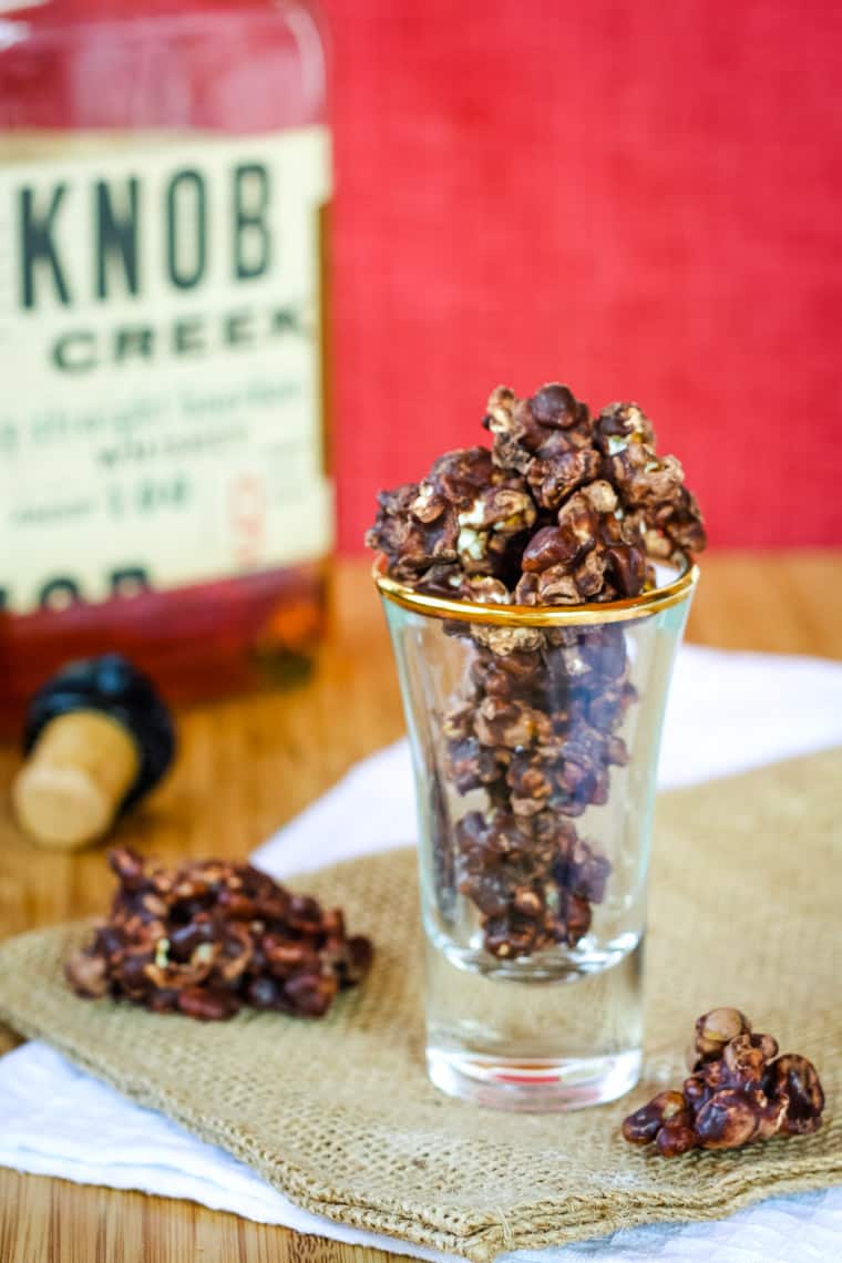 A shot glass filled with popcorn and pecans covered in bourbon-infused chocolate