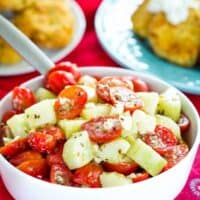 A white bowl of Cucumber Tomato Feta Salad on a table with red cloth napkins.