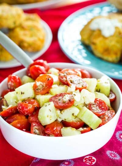 A white bowl of Cucumber Tomato Feta Salad on a table with red cloth napkins.