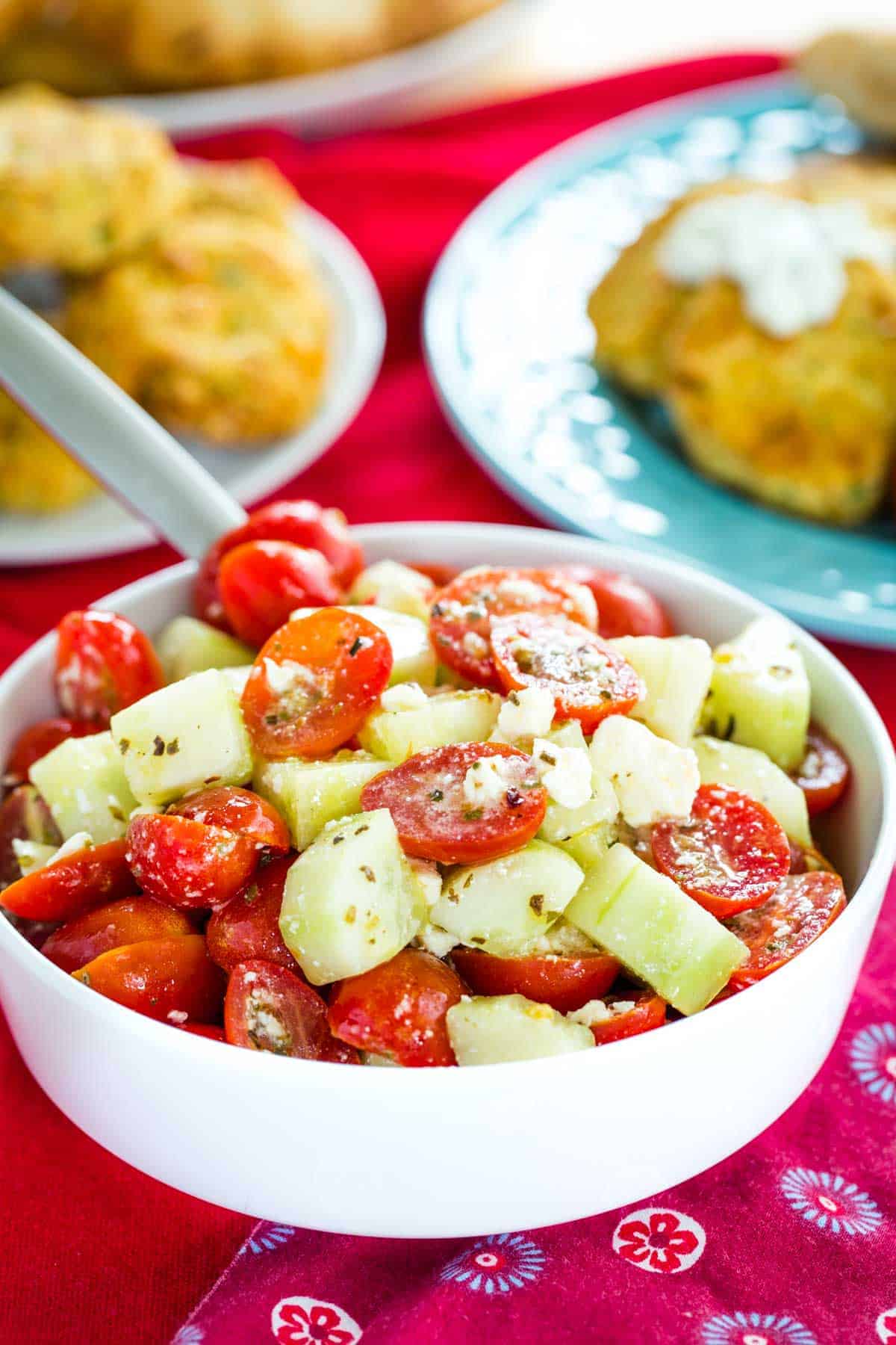 A white bowl of Cucumber Tomato Feta Salad on a table with red cloth napkins.