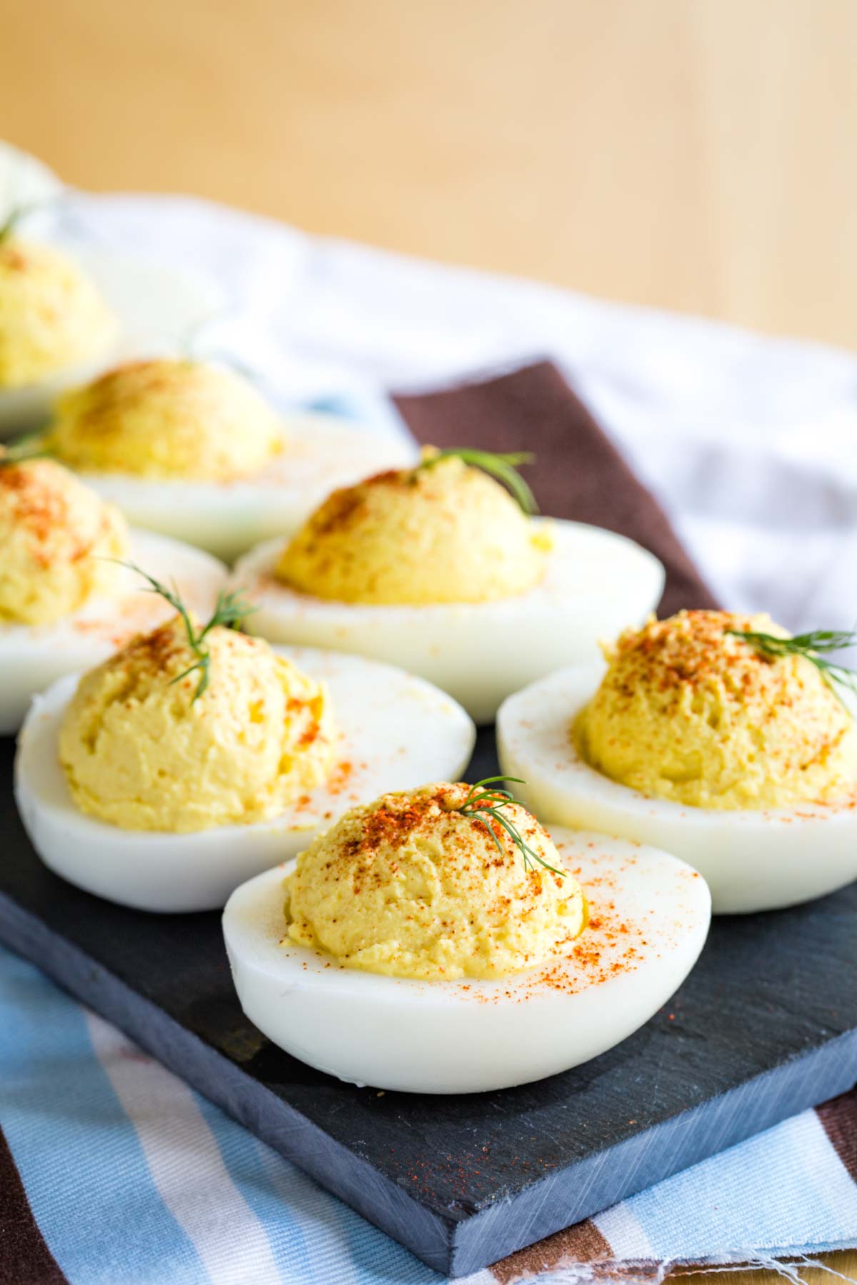 Greek Yogurt Deviled Eggs garnished with paprika and dill on a slate tray on top of a striped cloth napkin.
