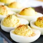 A closeup of a Deviled Egg garnished with paprika and dill with more blurred int he background on a platter.