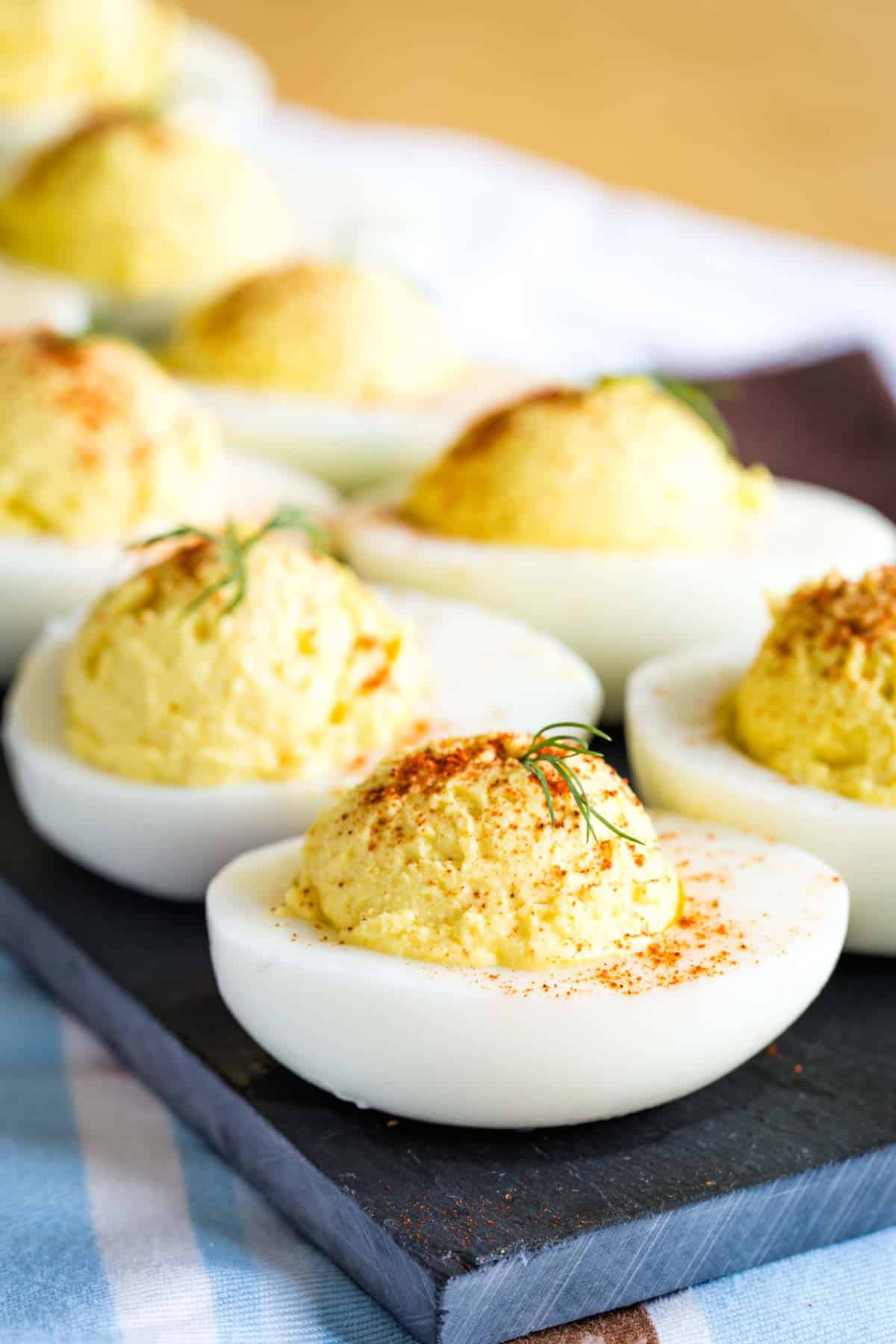 A closeup of a Deviled Egg garnished with paprika and dill with more blurred int he background on a platter.
