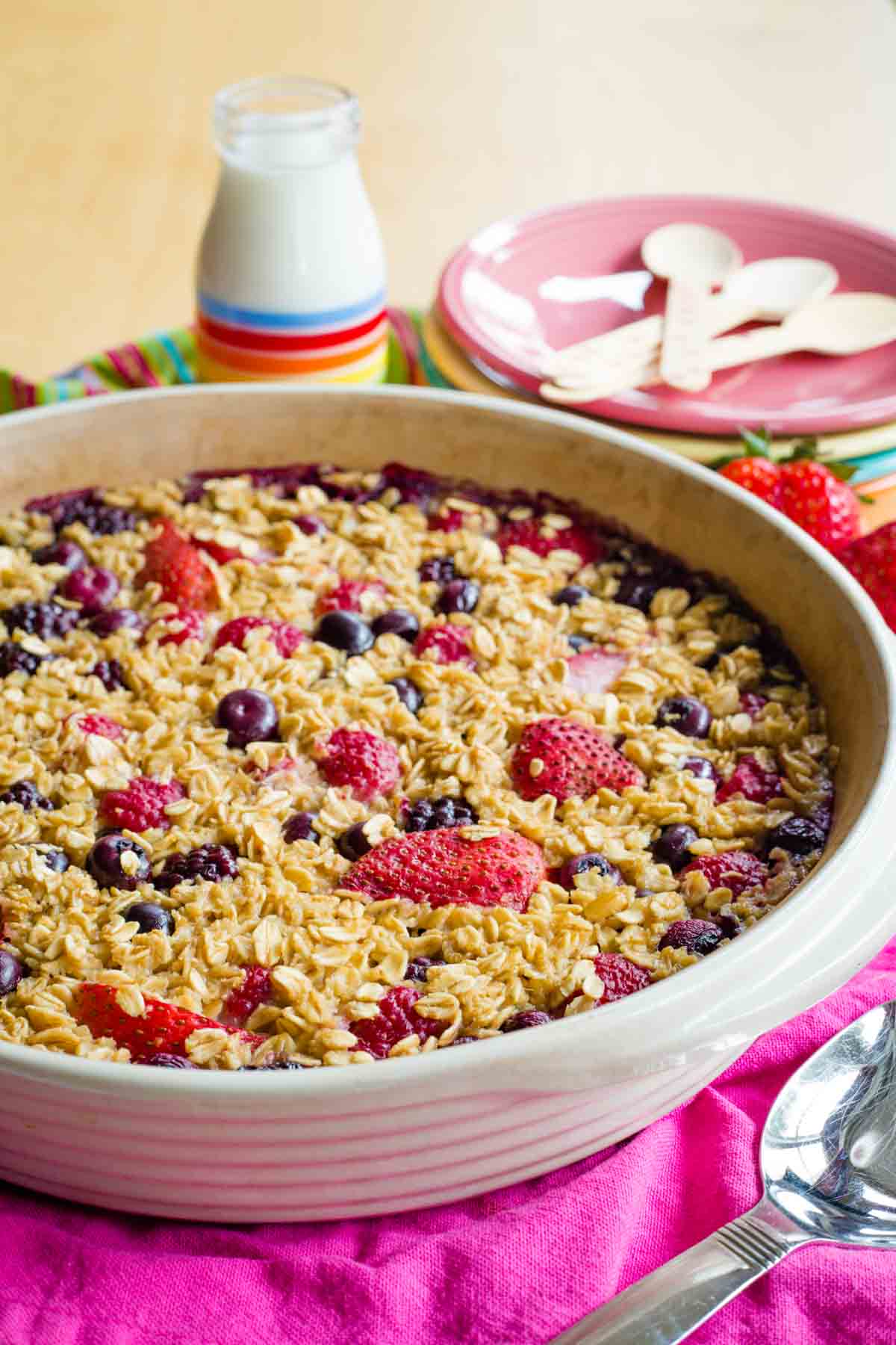 Round baking dish with Baked Oatmeal with various mixed berries on a pink cloth napkin with a serving spoon.