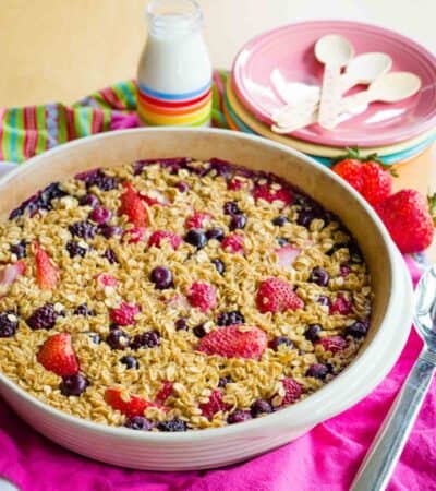 Berry Oatmeal Bake in a round pan on a stack of pink napkin, white, and striped cloth napkins.