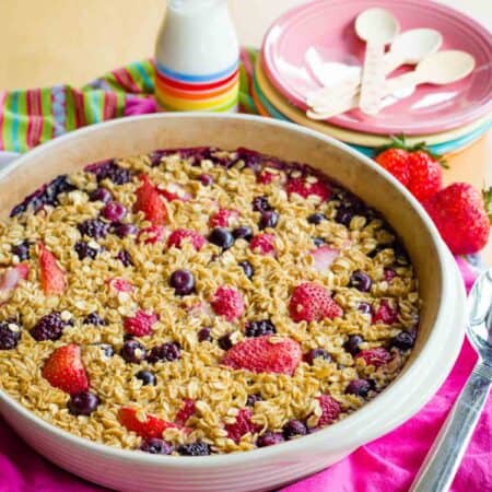 Berry Oatmeal Bake in a round pan on a stack of pink napkin, white, and striped cloth napkins.