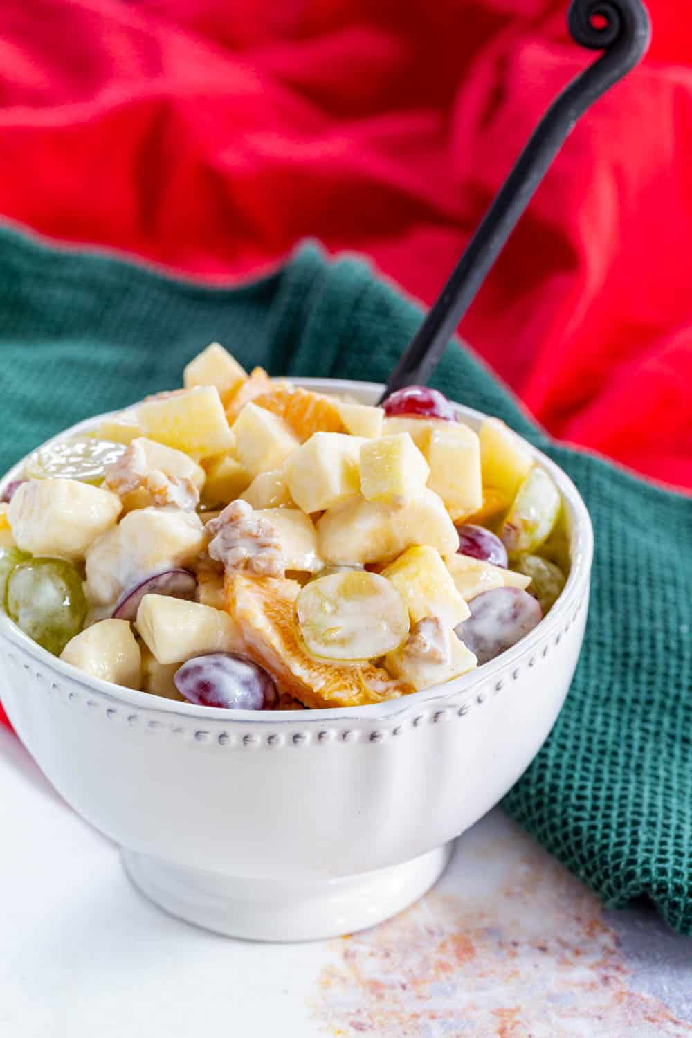 A decorative serving bowl of Winter Fruit Salad with a yogurt dressing on a table with red and green cloth napkins.