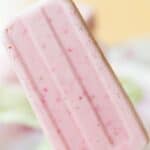 A pink popsicle being held up with text overlay that says "Strawberry Cheesecake Frozen Yogurt Popsicles".