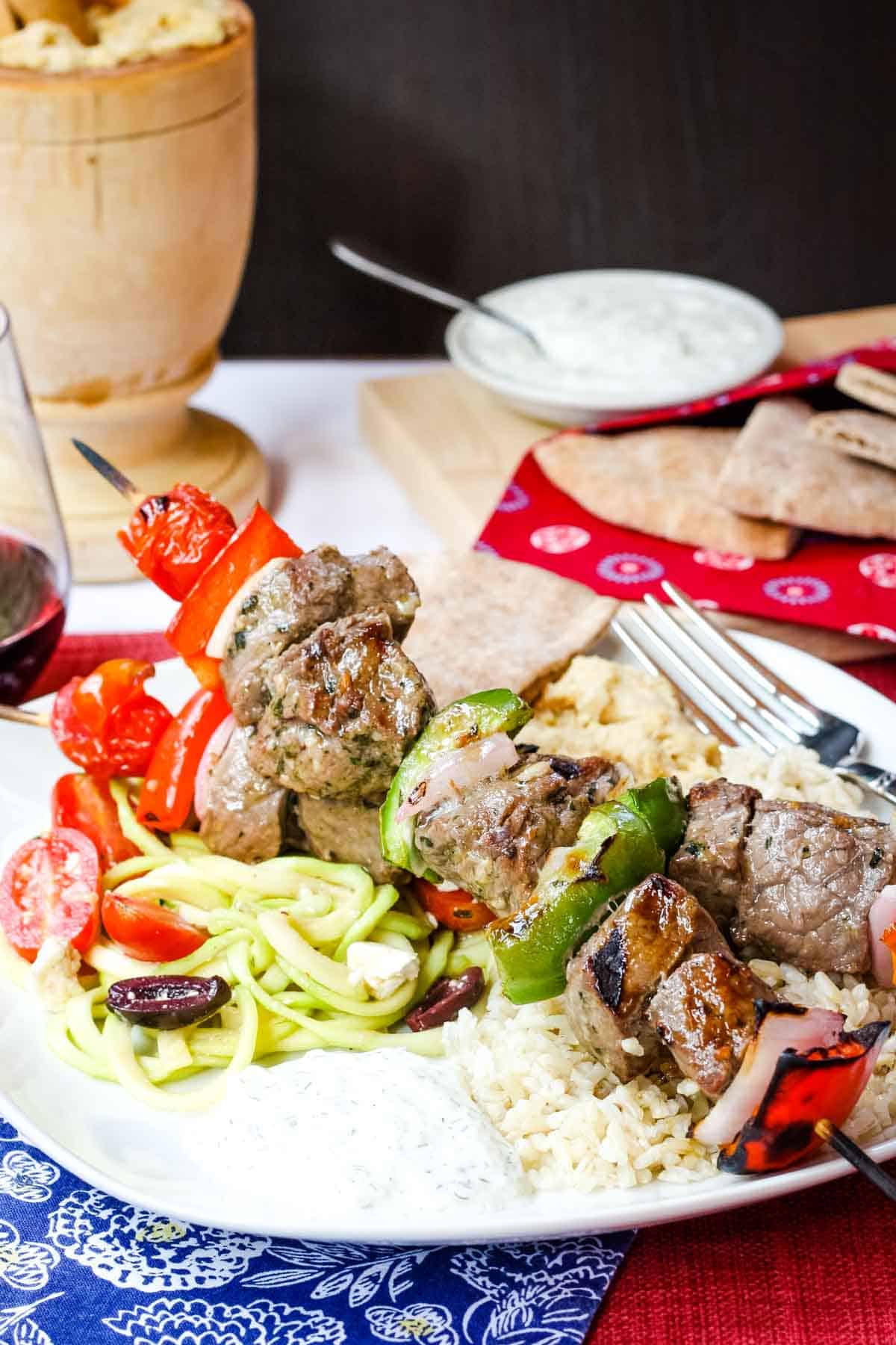 Grilled Greek Beef Souvlaki on a plate with rize, zoodles, pita, and tzatziki.