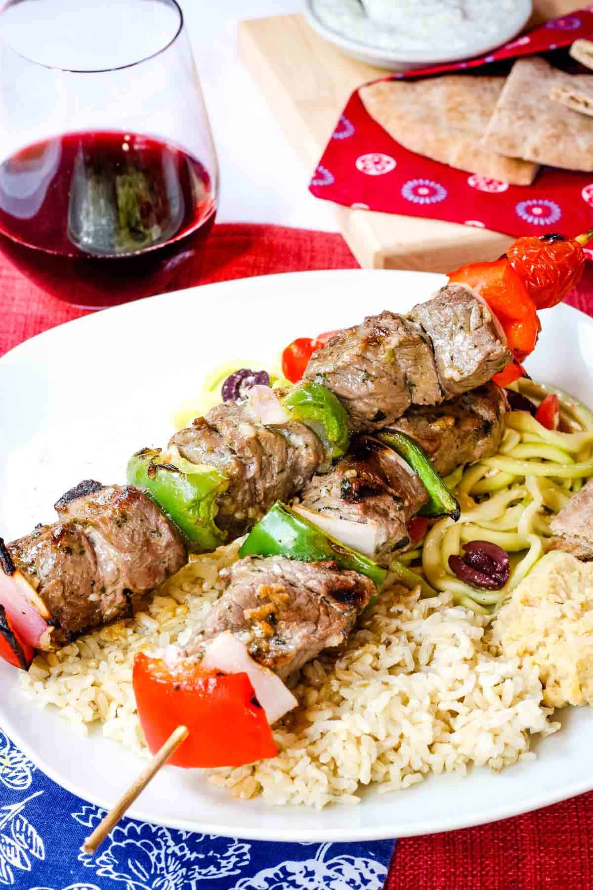 Gettk Beef kabobs with peppers an onions served over rice next to a glass of wine.