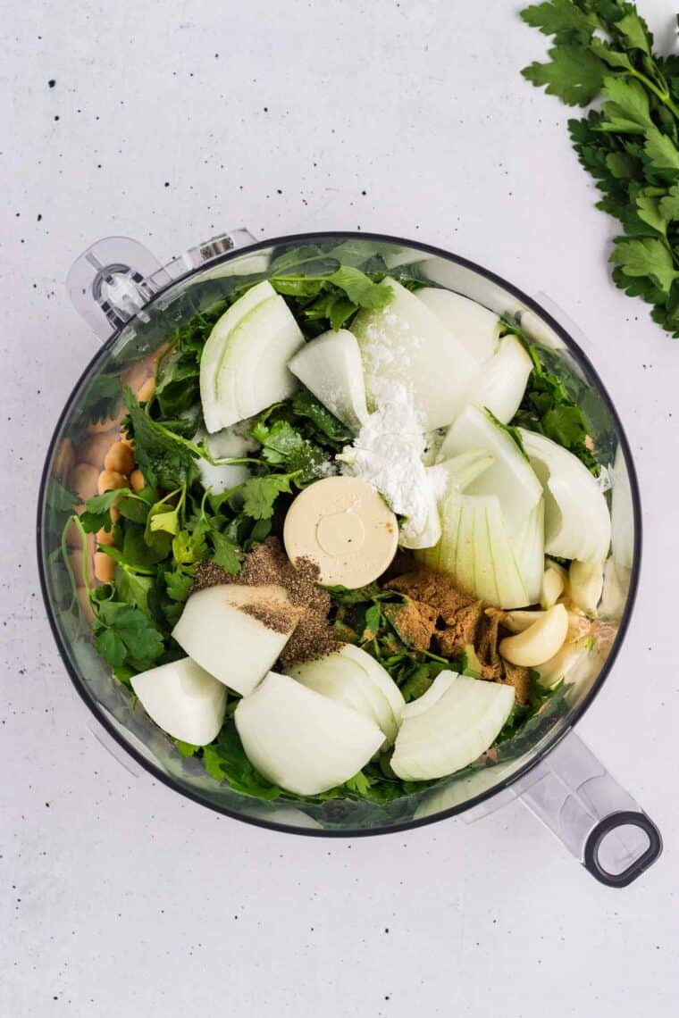 Herbs, onions, garlic, and spices added to a food processor with chickpeas