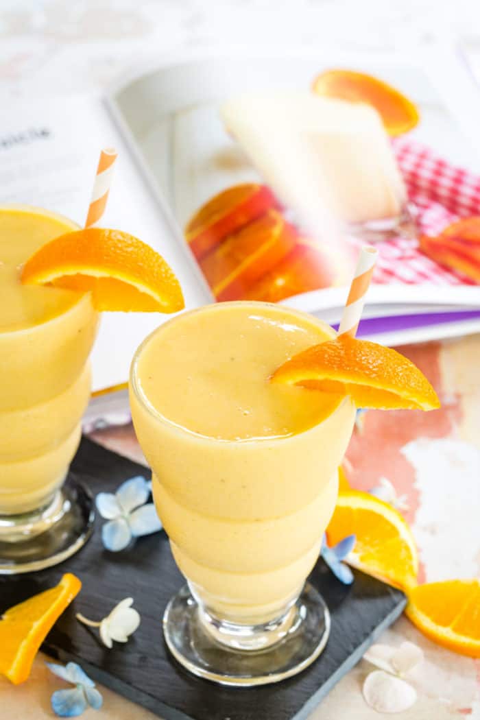 Two Orange Creamsicle Smoothies plus open to a page in The Protein Smoothie Bible cookbook