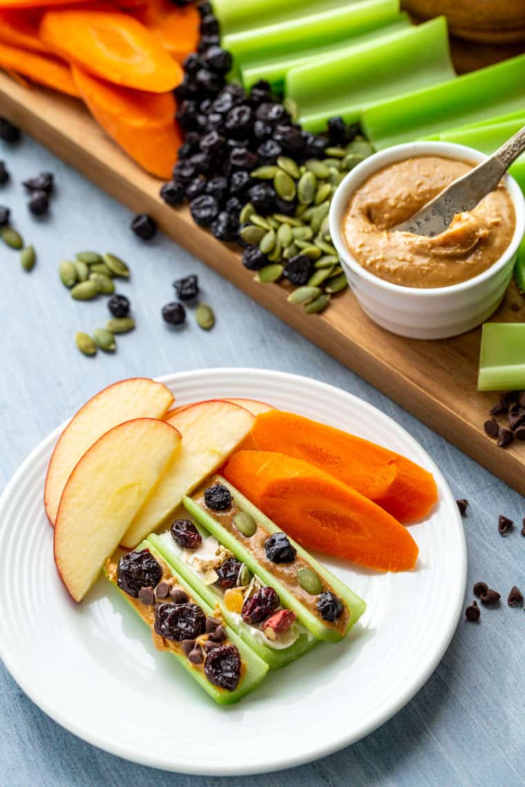 A white plate with creative Ants on a Log with carrots and apples