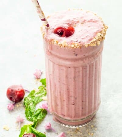 A light pink Cherry Smoothie in a decorative glass with a straw.