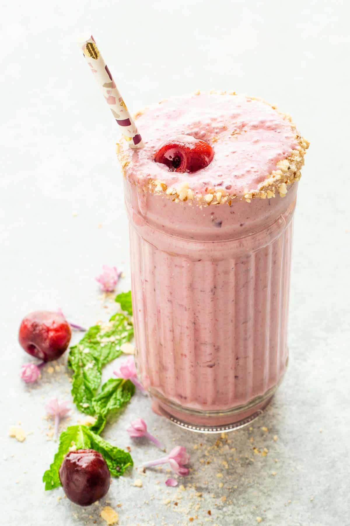 A light pink Cherry Smoothie in a decorative glass with a straw.