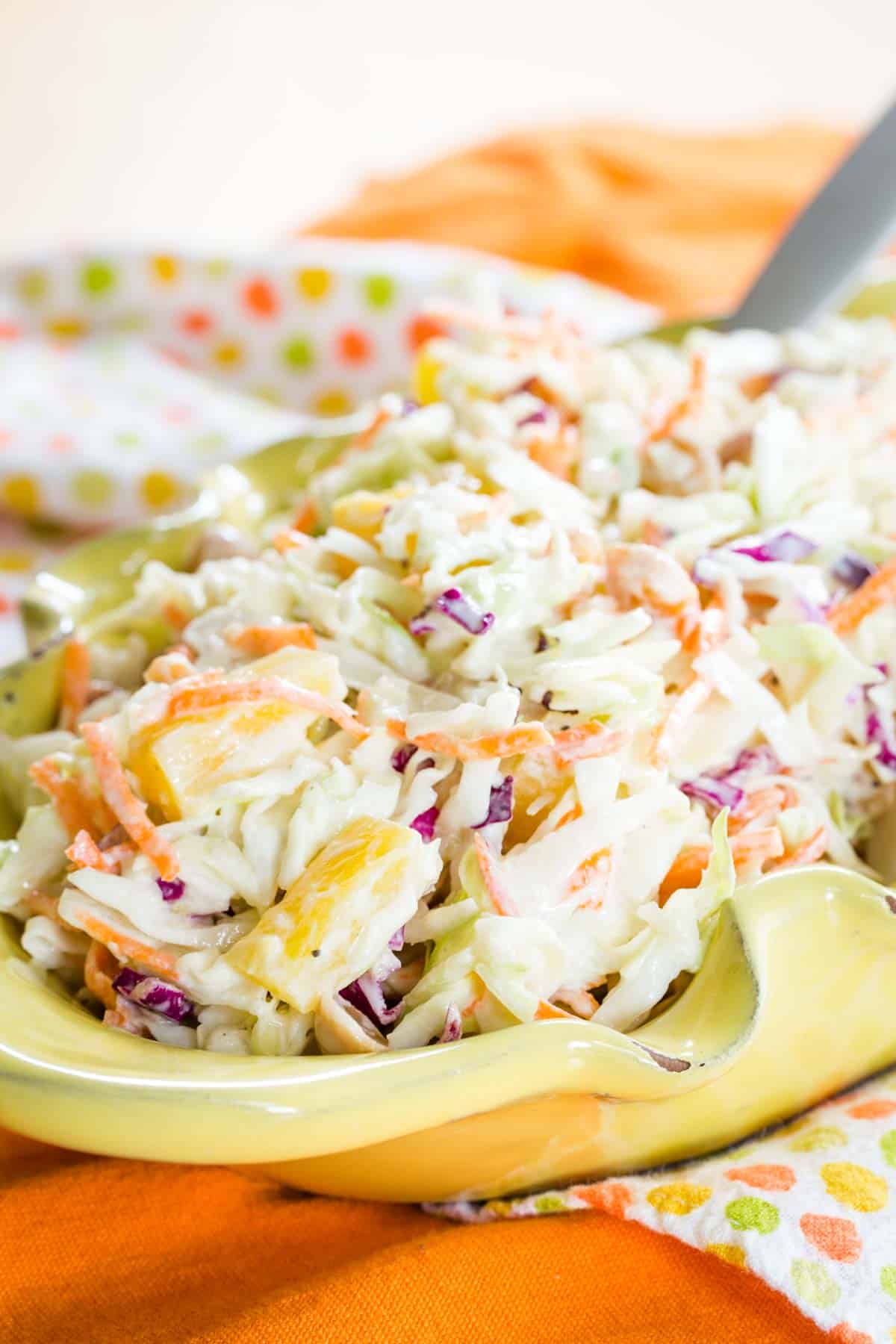 Hawaiian Pineapple Coleslaw in a serving bowl with a spoon in it on top of brightly colored cloth napkins.