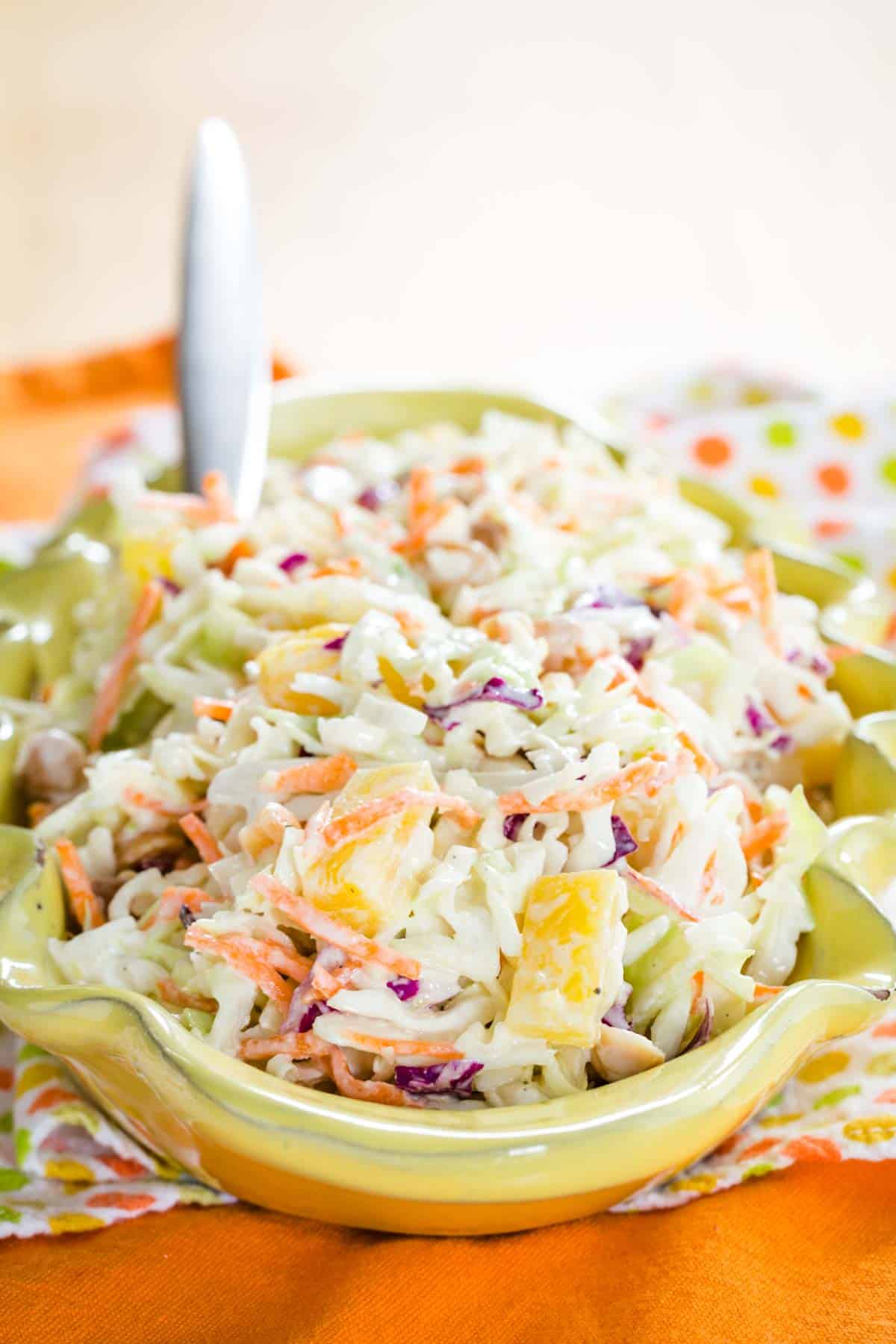 A front view of Pineapple Coleslaw in a yellow serving dish with a spoon in the back of it.
