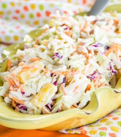 Hawaiian Coleslaw with pineapple in a yellow bowl on a polka dot and orange cloth napkins.