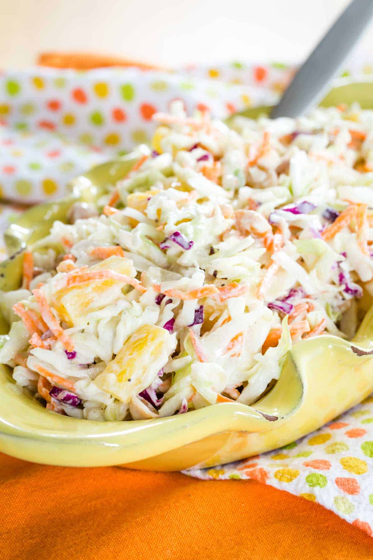 Hawaiian Coleslaw with pineapple in a yellow bowl on a polka dot and orange cloth napkins.