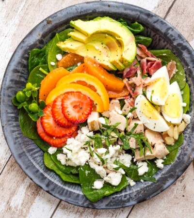 Strawberry Avocado Spinach Salad on a tin plate with antique fork and mustard-colored napkin