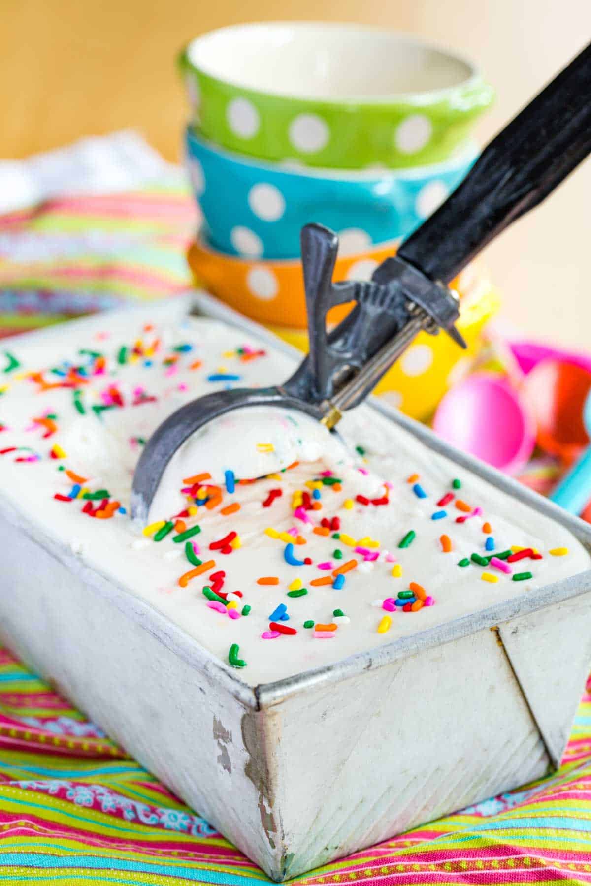 A scoop in a container of Cake Batter Ice Cream topped with rainbow sprinkles.