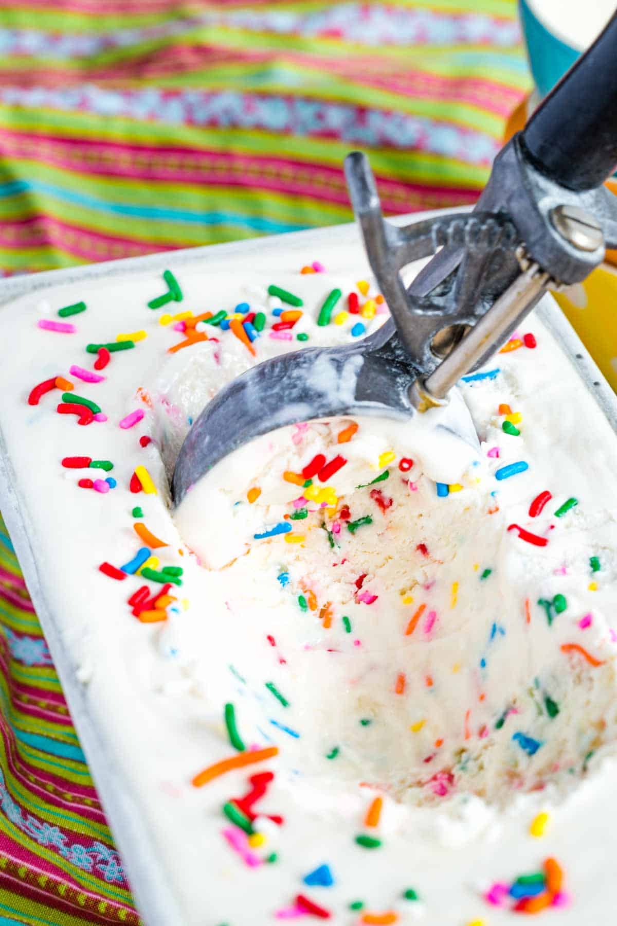 Overhead of scoop in a container of Gluten Free Birthday Cake Ice Cream with Rainbow Sprinkles.