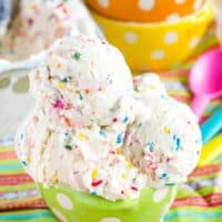No-Churn Birthday Cake Ice Cream in a green polka dot bowl on top of a colorful striped cloth napkin.