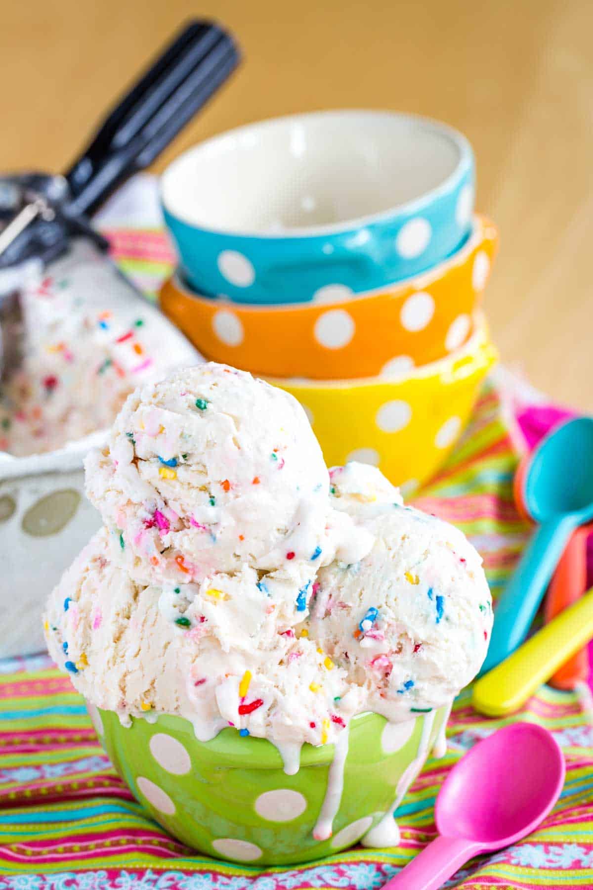 Cake Batter Ice Cream in a green polka dot bowl with a pink spoon next to it and more colorful bowls and spoons in the background.