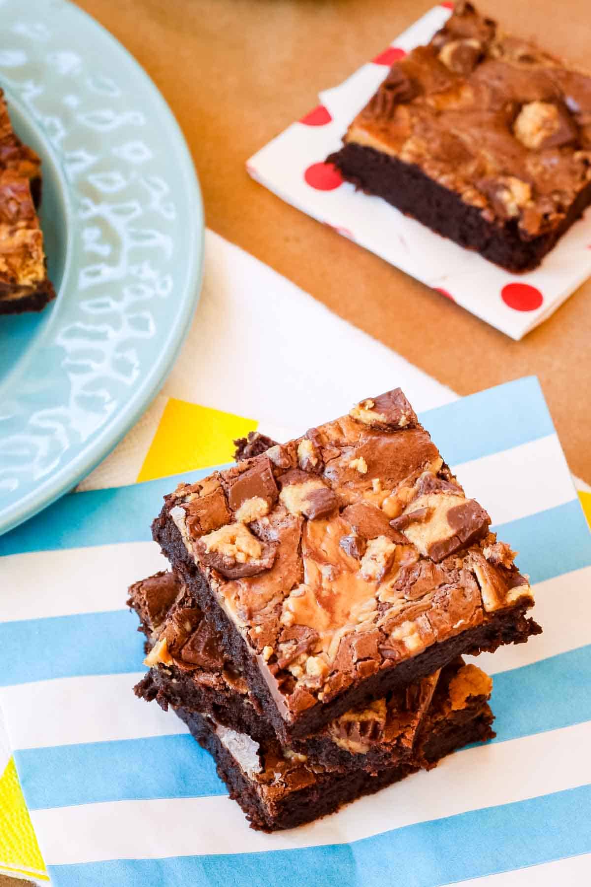 Three peanut butter brownies stacked on a blue and white striped napkin, with a second brownie on a polka dot napkin in the background.