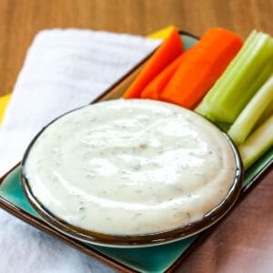 A small bowl of Greek Yogurt Ranch Dip with carrot and celery sticks next to it.