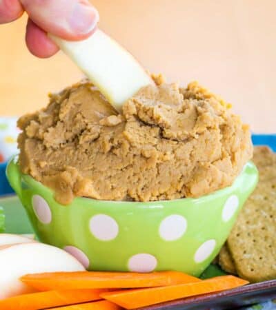 Peanut Butter Cookie Dough Dip with an apple slice being dipped into it surrounded by apples, carrots, and graham crackers on a platter.