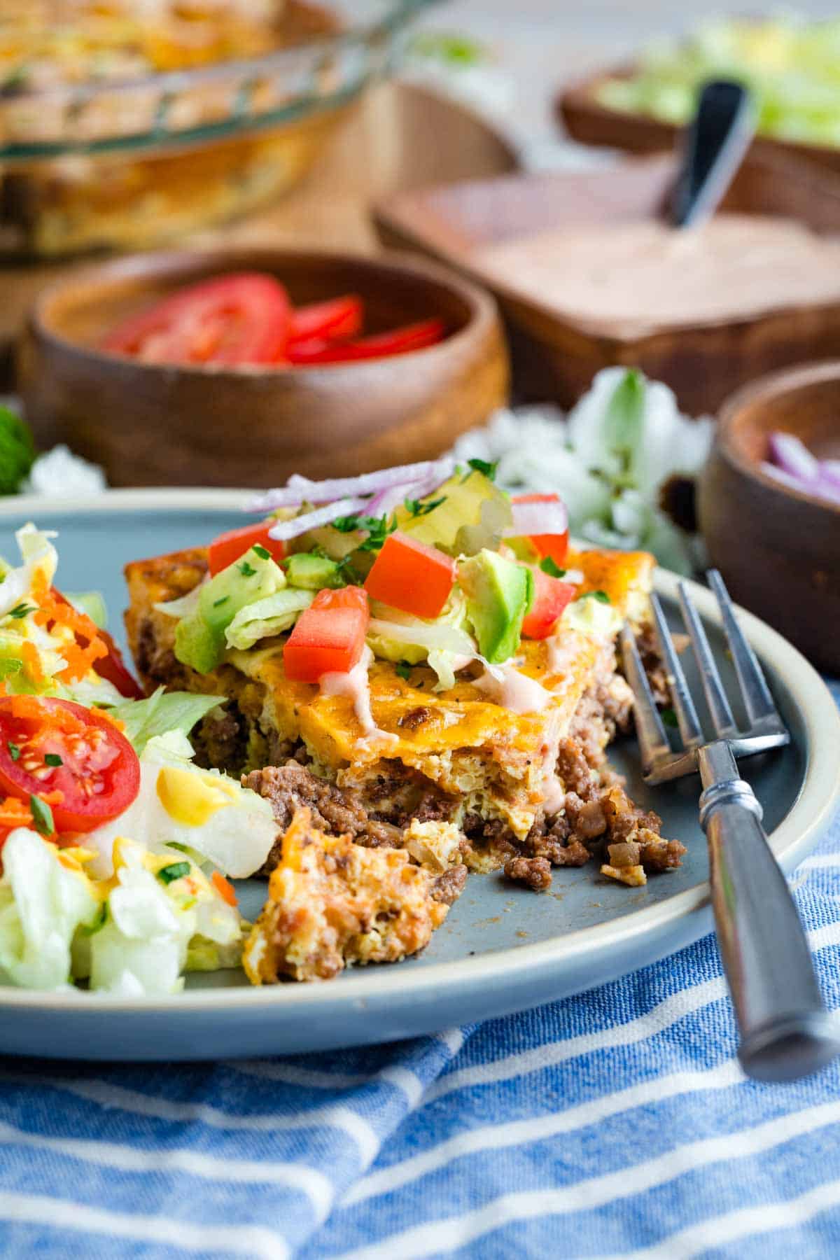 Bacon Cheeseburger Crustless Quiche is made with ground beef, bacon, and cheese, plus your favorite burger toppings. A fork on a plate with a slice of bacon cheeseburger crustless quiche