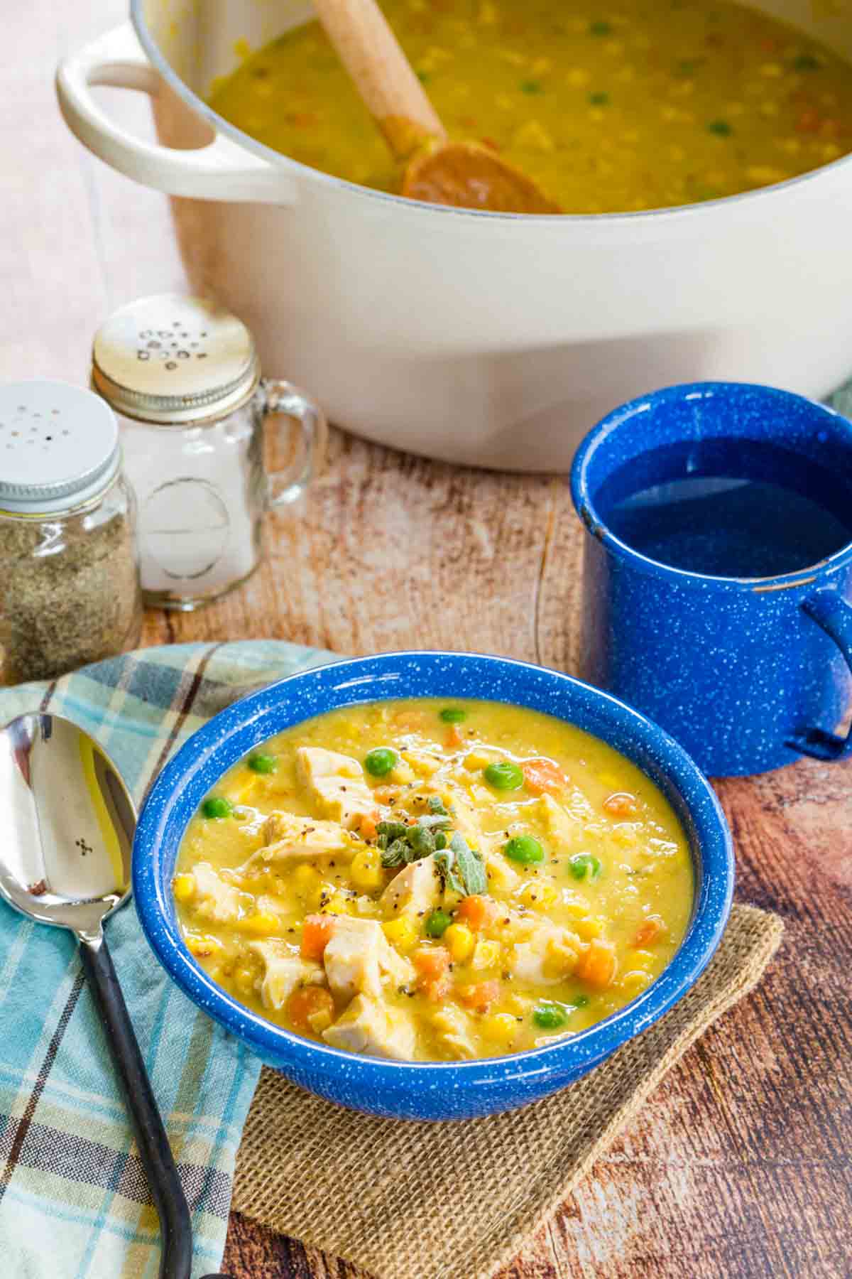 A blue bowl filled with Chicken Corn Chowder from a pot sitting in background.