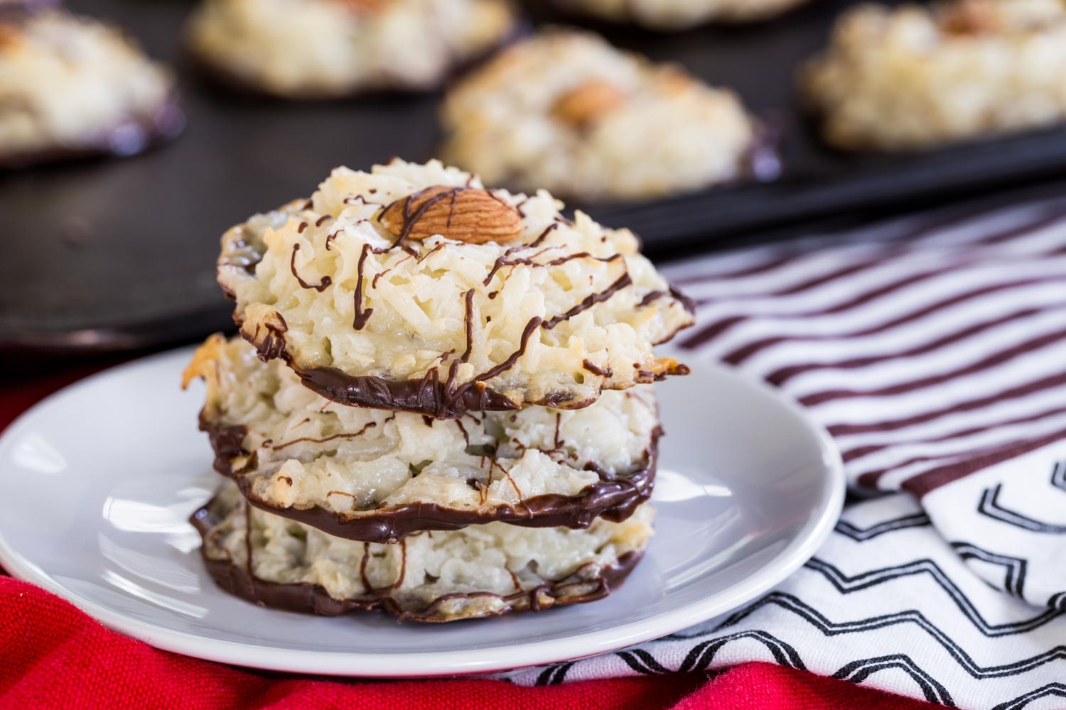 A stack of three Almond Joy Cookies on a small white plate with more on the cookie sheet behind it.