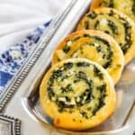 A row of appetizer pinwheels on a silver platter on top of blue and white cloth napkins with text overlay that says "Spinach Feta Pinwheels".
