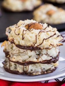 A stack of three Almond Joy Cookies on a small white plate with more on the cookie sheet behind it.