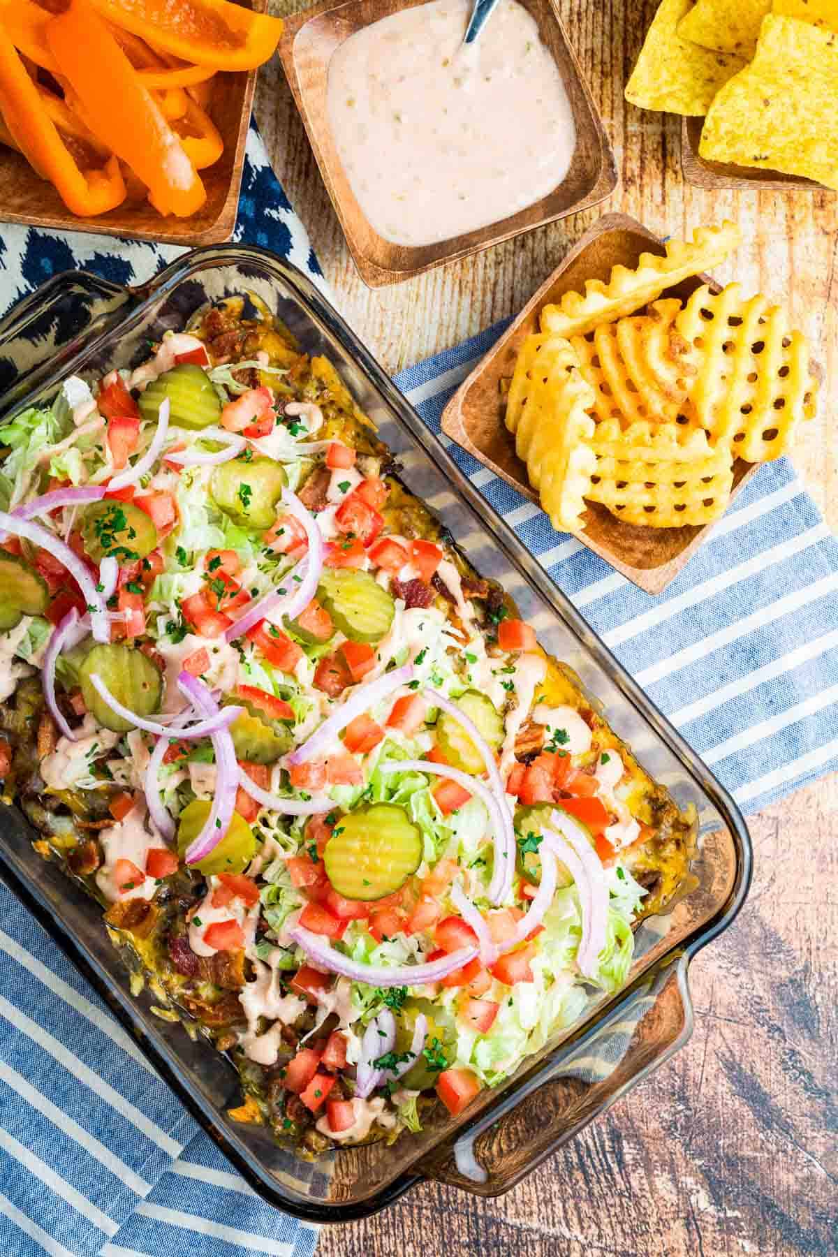 Overhead view of a baking dish of bacon cheeseburger dip next to waffle fries