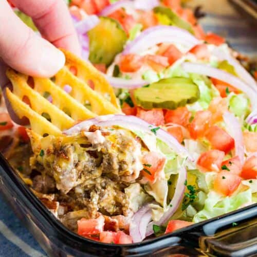 A hand dipping a waffle fry into bacon cheeseburger dip