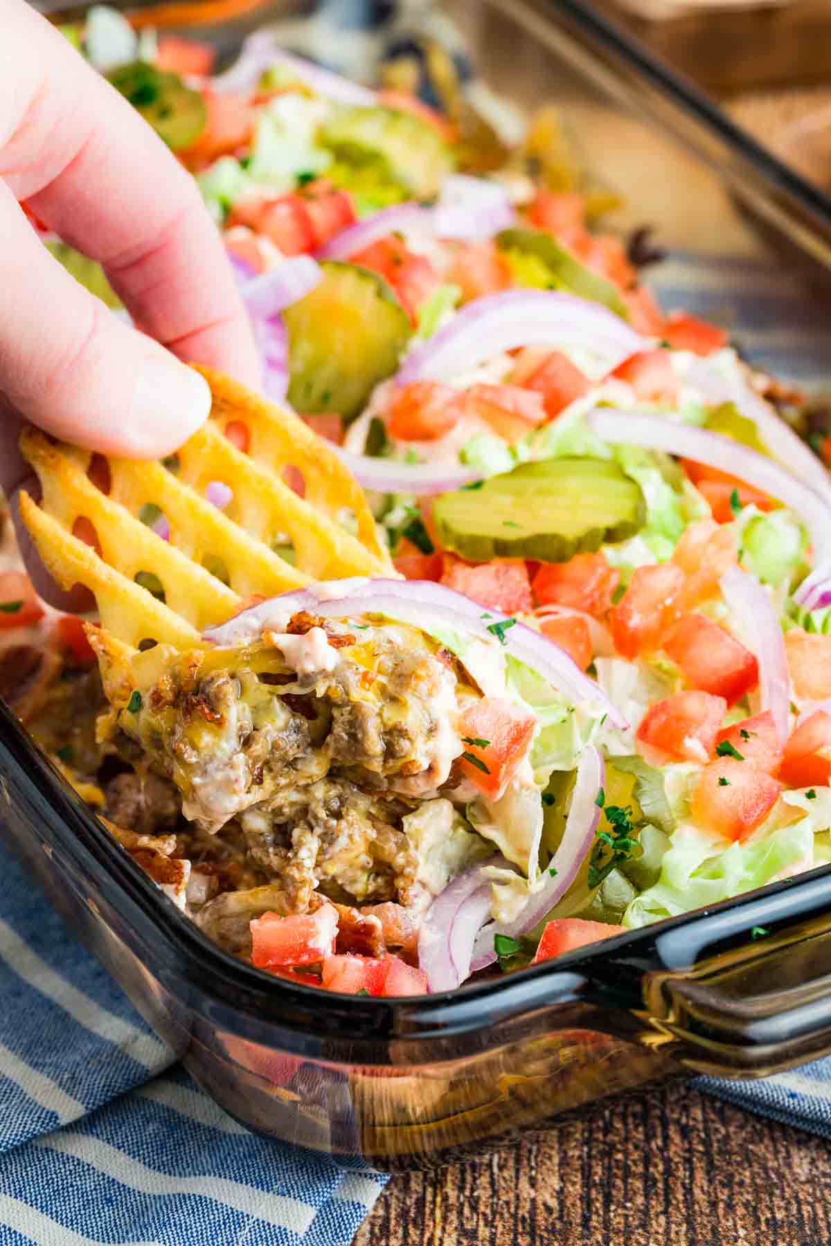 A hand dipping a waffle fry into bacon cheeseburger dip