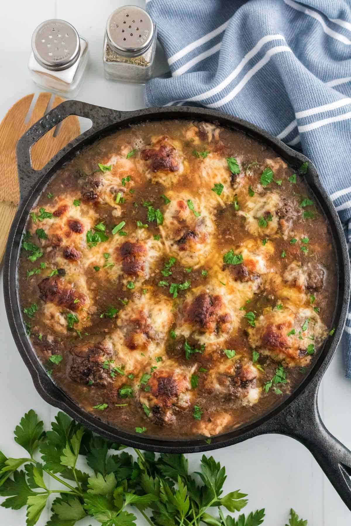 French onion meatballs topped with broiled cheese in a skillet.