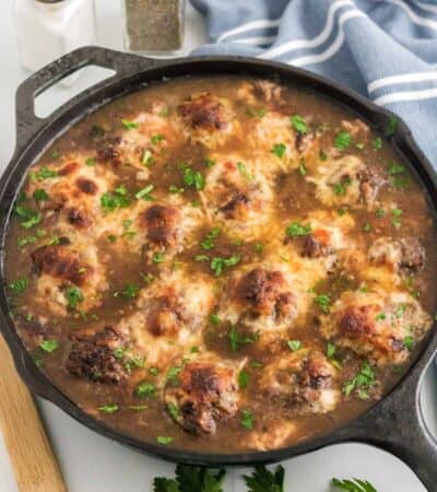 French onion meatballs topped with broiled cheese in a skillet.