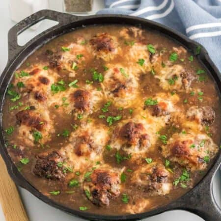 French onion meatballs topped with broiled cheese in a skillet.