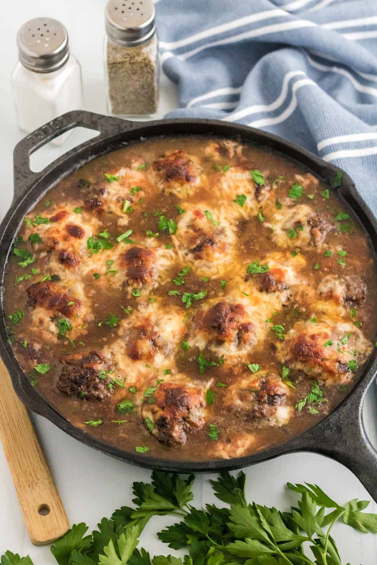 French onion meatballs topped with broiled cheese in a skillet.