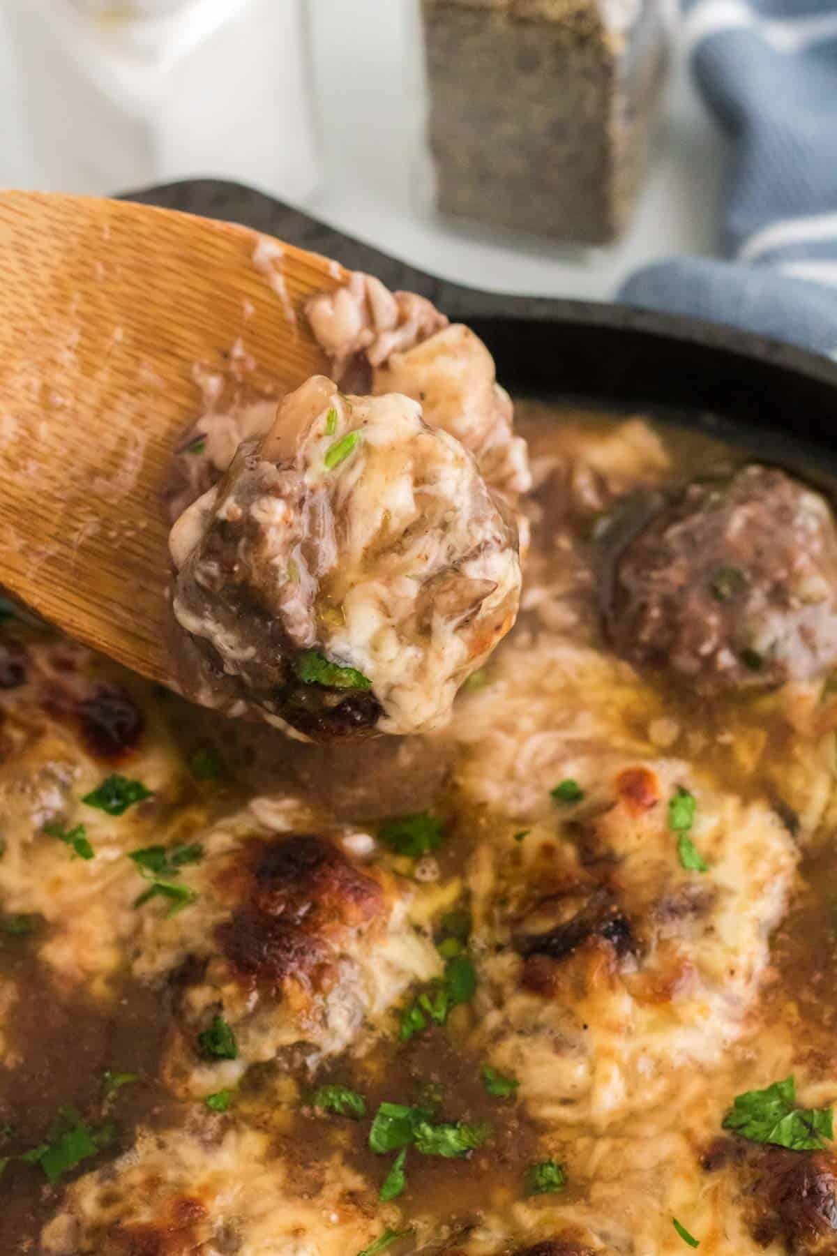 Close up of a French onion meatball scooped up with a wooden spoon.