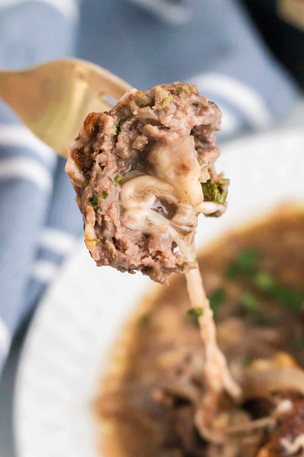 A mozzarella stuffed meatball cut in half to reveal the cheesy center.