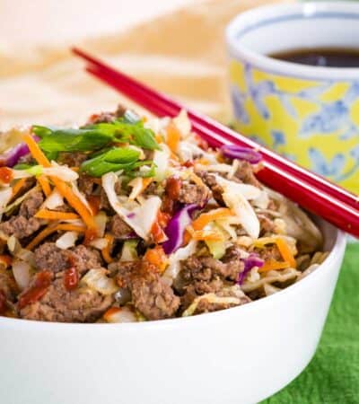 Egg roll in a bowl with a pair of red chopsticks, topped with scallions.