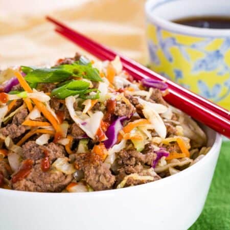 Egg roll in a bowl with a pair of red chopsticks, topped with scallions.