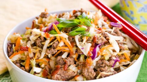 A Beef Egg Roll Bowl with a pair of red chopsticks, topped with scallions.