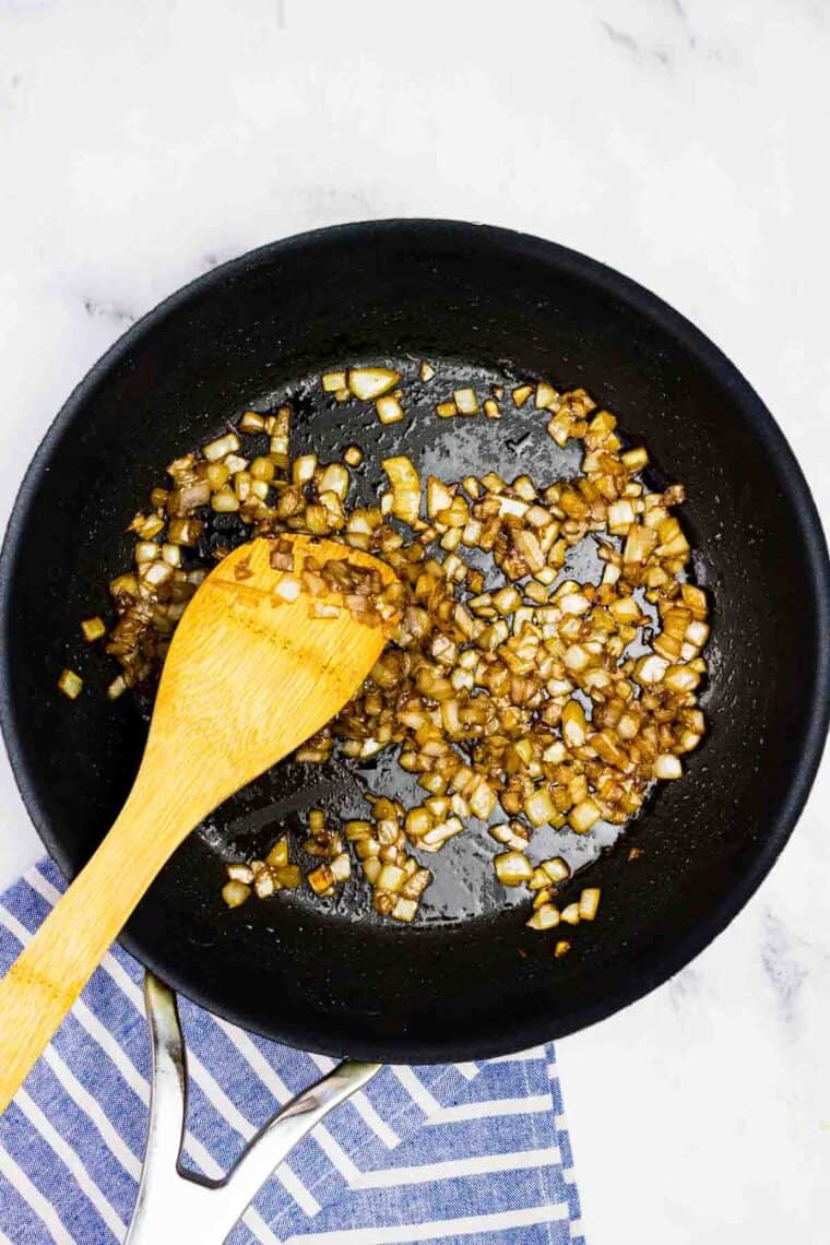 A wooden spoon sauteing onions