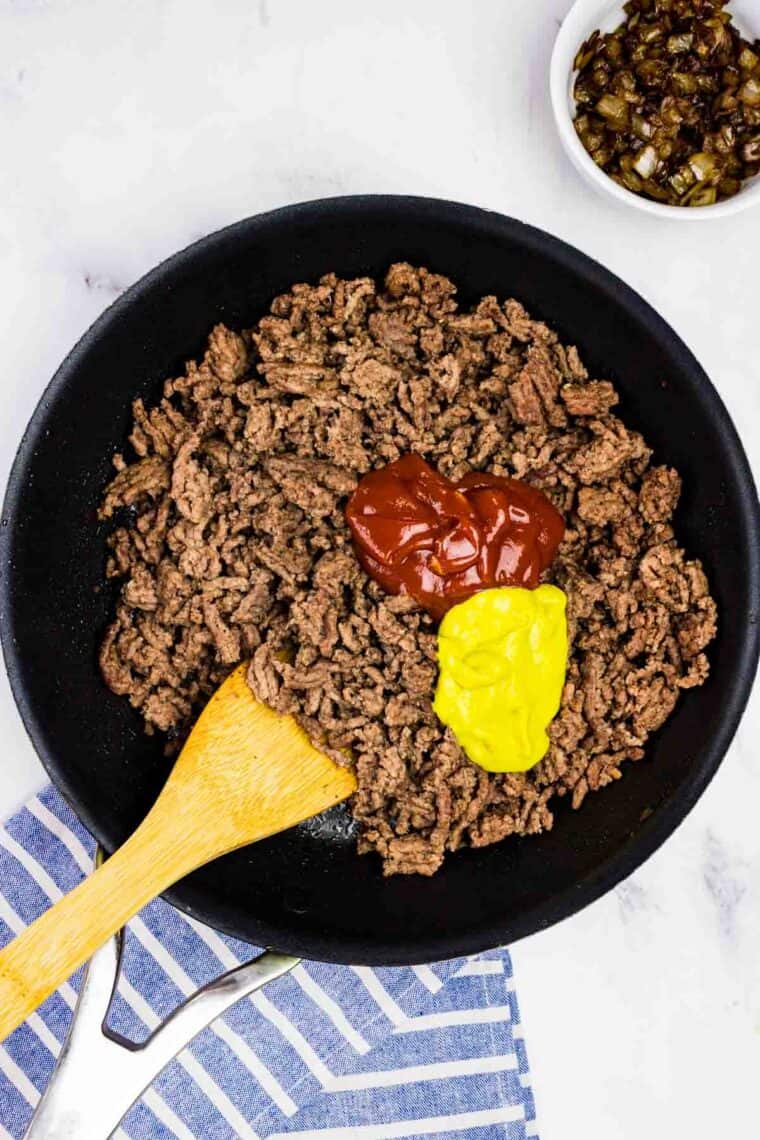 Adding ketchup and mustard to ground beef in a skillet